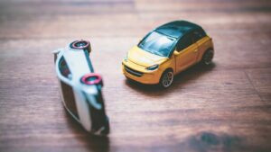 Two toy cars on a wooden desk, illustrating a collision, symbolizing factors that determine the severity of auto accident injuries