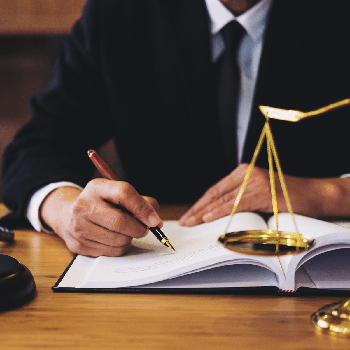 Close-up of a personal injury lawyer writing in a ledger or signing a settlement, with a partial view of the scale of Justice, symbolizing the dedication to legal representation by Kevin R. Hansen, Personal Injury Lawyer in Las Vegas