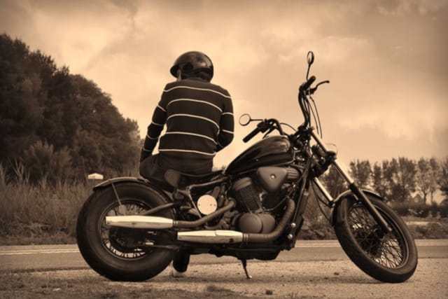 Man leaning on a street bike with a dark overlay and cloudy background, evoking the resilience and determination of motorcycle accident victims represented by Kevin R. Hansen, Motorcycle Accident Lawyer in Las Vegas